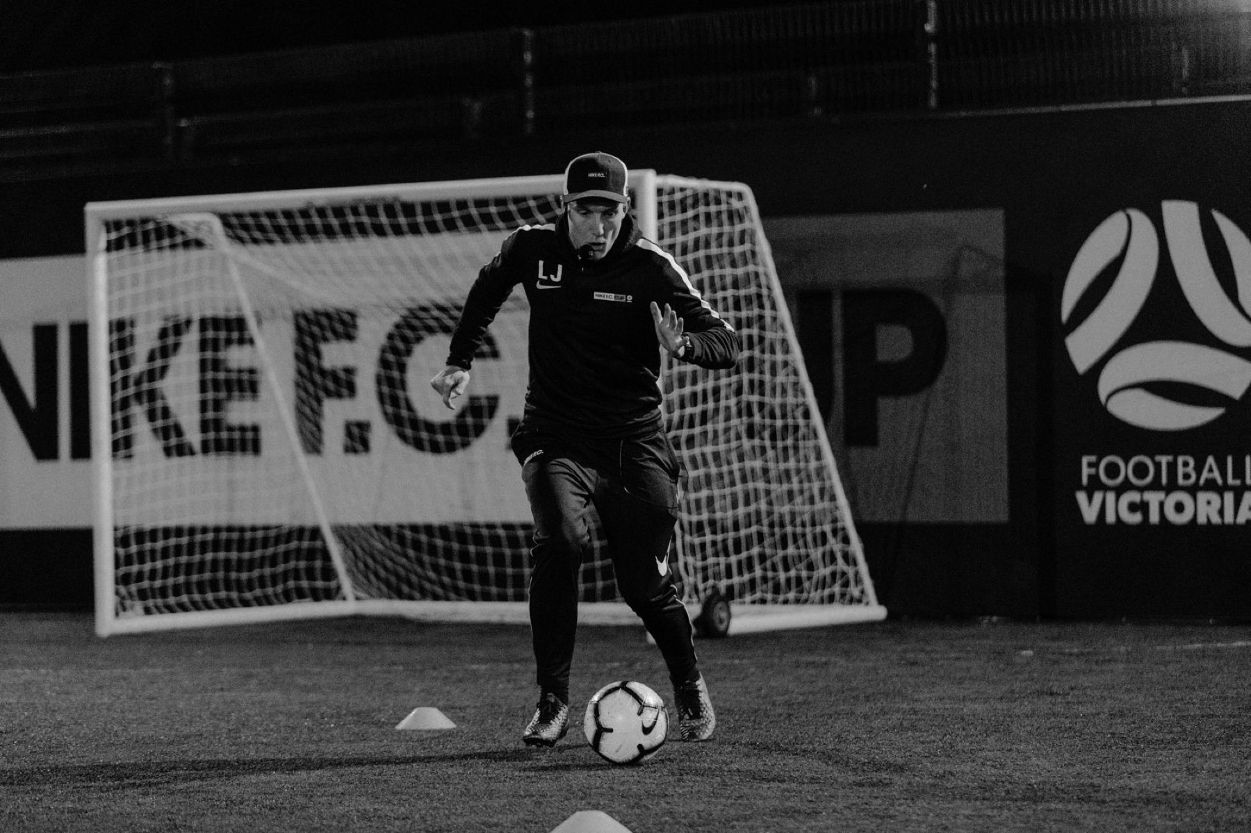 Black and white photo of Lee driving the ball forward at a Nike FC night session